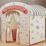 Casuta de joaca pentru copii Nichiduta Garden Pink Bakery, iluminata, intrare eleganta cu perdelele, polita laterala, constructie robusta, margini rotunjite, dimensiune 115 x 92 x 98 cm